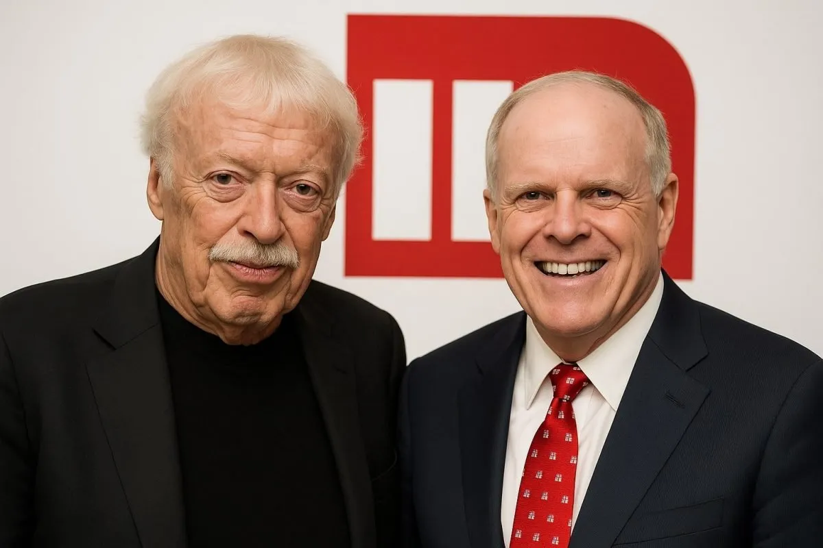 John Hennessy (à droite), ancien président de l'université de Stanford, et Phil Knight (à gauche), co-fondateur de Nike, posent ensemble devant un fond avec un logo rouge et blanc. Les deux figures emblématiques sont les financeurs de la bourse Knight-Hennessy Scholars.